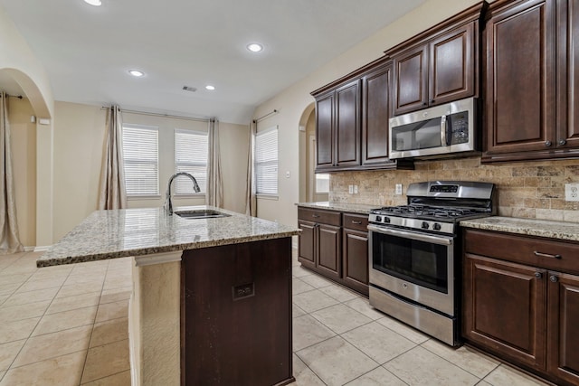 19214 S Cottonwood Green Ln, Cypress, TX 77433 - kitchen featuring appliances with stainless steel finishes, a sink, arched walkways, light tile patterned flooring, and decorative backsplash