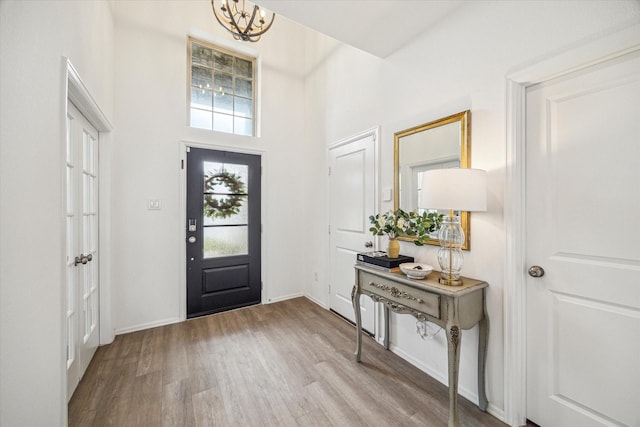 foyer featuring an inviting chandelier, baseboards, a high ceiling, and wood finished floors
