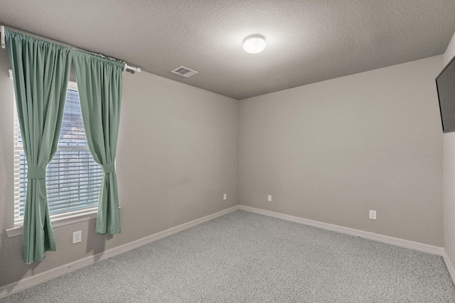 carpeted spare room featuring baseboards, visible vents, and a textured ceiling