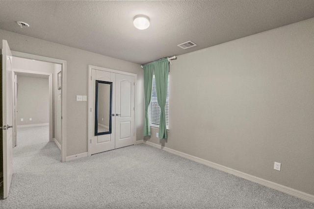 unfurnished bedroom featuring a textured ceiling, baseboards, visible vents, and light carpet