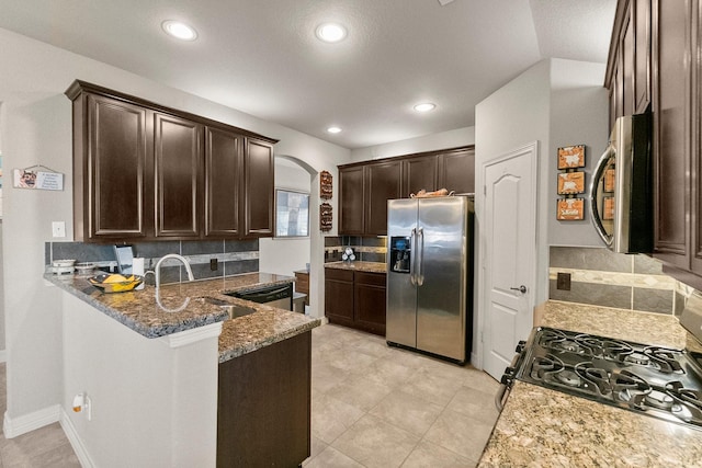 kitchen featuring tasteful backsplash, dark brown cabinets, appliances with stainless steel finishes, arched walkways, and stone countertops