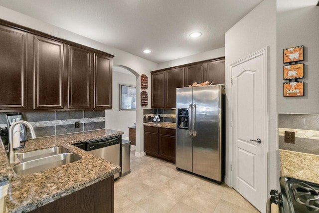 kitchen featuring arched walkways, a sink, dark brown cabinetry, appliances with stainless steel finishes, and tasteful backsplash