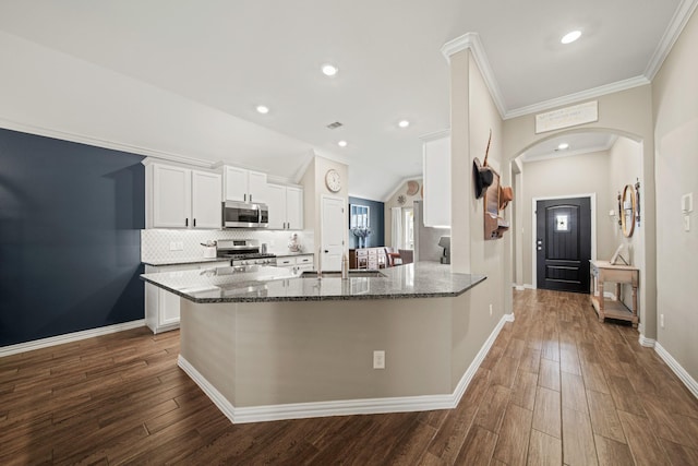 kitchen with a sink, dark stone countertops, stainless steel appliances, arched walkways, and white cabinets