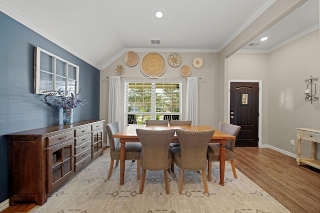 dining space with visible vents, baseboards, ornamental molding, vaulted ceiling, and light wood-style flooring