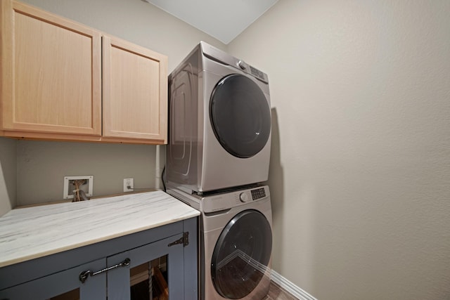 laundry area with cabinet space, stacked washing maching and dryer, and baseboards