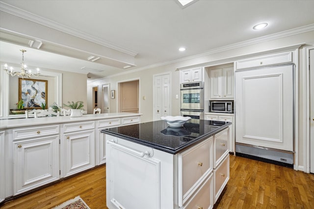 kitchen with a kitchen island, appliances with stainless steel finishes, wood finished floors, a notable chandelier, and white cabinets