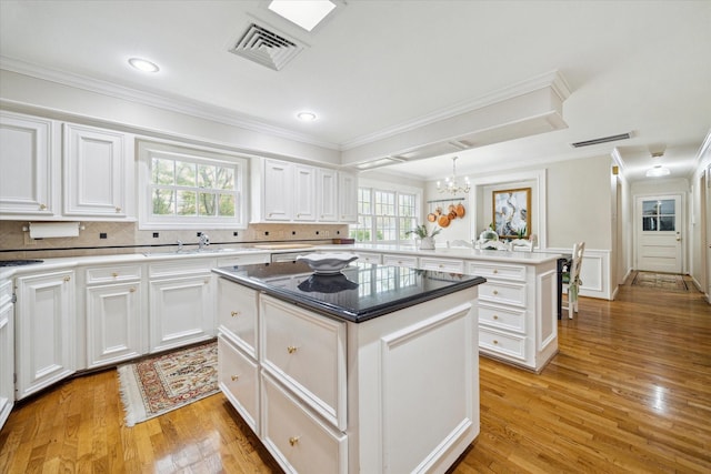 kitchen featuring visible vents, a kitchen island, an inviting chandelier, a peninsula, and white cabinets