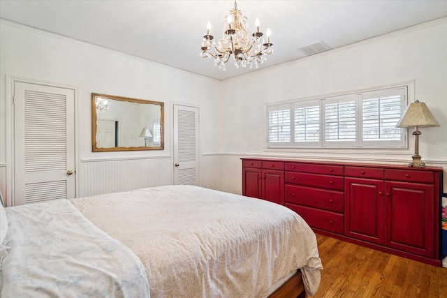 bedroom featuring visible vents, an inviting chandelier, wood finished floors, and crown molding