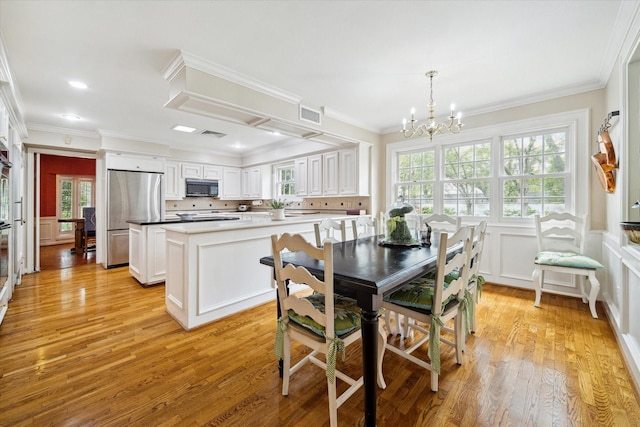 dining room with visible vents, a wainscoted wall, light wood-type flooring, ornamental molding, and an inviting chandelier