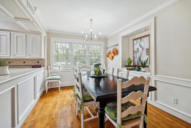 dining area with an inviting chandelier, light wood-style flooring, crown molding, and a decorative wall