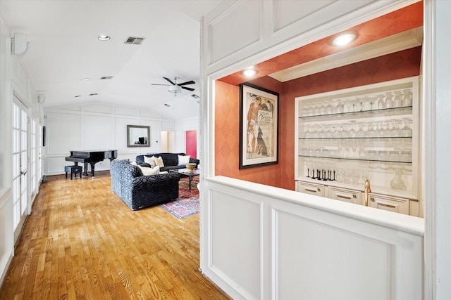 corridor with lofted ceiling, a decorative wall, visible vents, and light wood finished floors