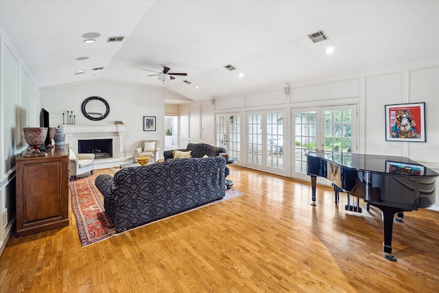 living area with visible vents, a fireplace with raised hearth, a decorative wall, ceiling fan, and vaulted ceiling