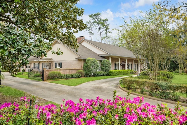 view of front of house featuring a gate, brick siding, driveway, and a chimney