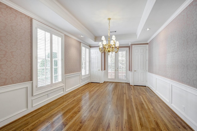 unfurnished dining area with a tray ceiling, a notable chandelier, wainscoting, and wallpapered walls