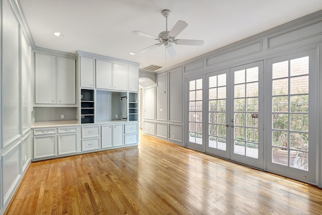 kitchen featuring a ceiling fan, light wood finished floors, arched walkways, light countertops, and a decorative wall