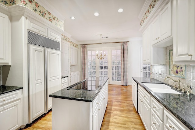 kitchen featuring light wood finished floors, crown molding, black electric stovetop, a chandelier, and a sink