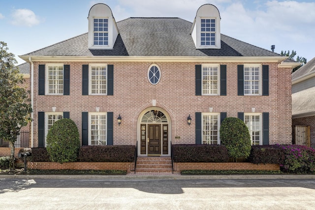 colonial house featuring brick siding and a shingled roof