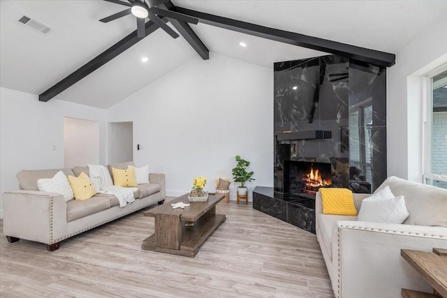 living room with visible vents, wood finished floors, a premium fireplace, ceiling fan, and vaulted ceiling with beams