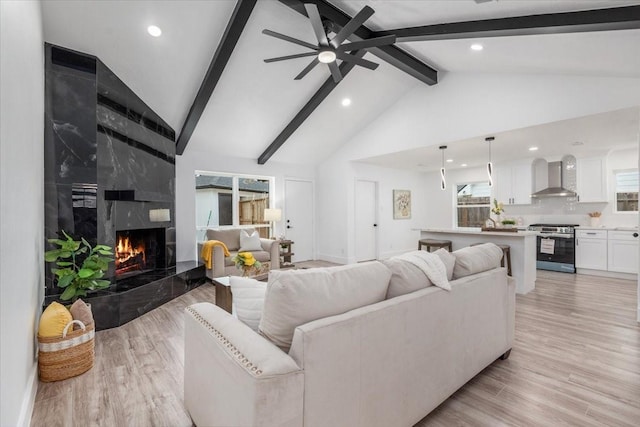 living area with a high end fireplace, ceiling fan, beam ceiling, light wood-style floors, and high vaulted ceiling