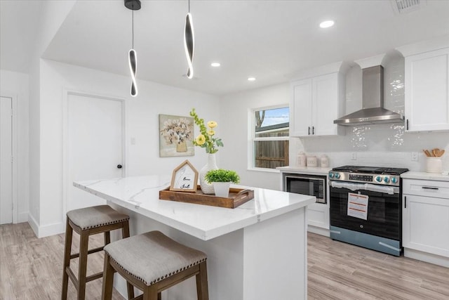 kitchen with backsplash, wall chimney range hood, light wood-style floors, white cabinets, and stainless steel appliances