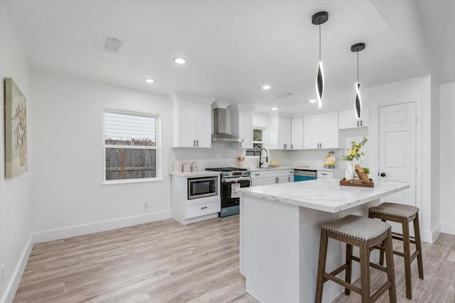 kitchen featuring visible vents, white cabinets, stainless steel appliances, wall chimney exhaust hood, and a sink