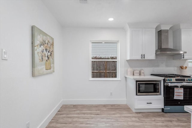 kitchen with light wood-style floors, appliances with stainless steel finishes, wall chimney exhaust hood, white cabinets, and decorative backsplash