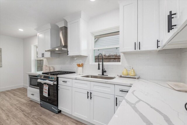 kitchen featuring a sink, stainless steel appliances, light wood-style floors, white cabinetry, and wall chimney exhaust hood