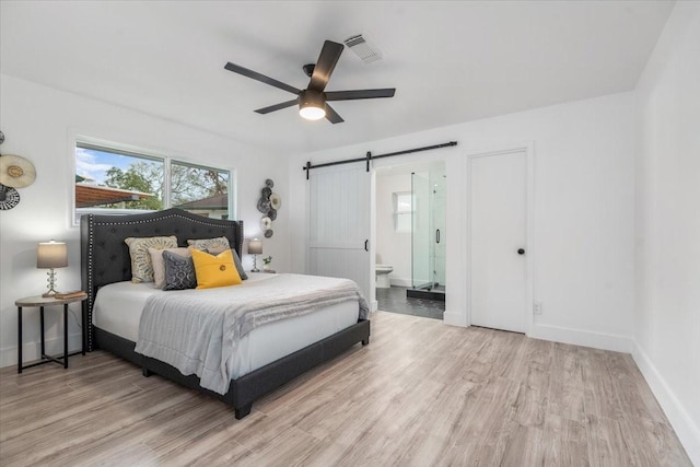 bedroom with wood finished floors, baseboards, visible vents, a barn door, and connected bathroom