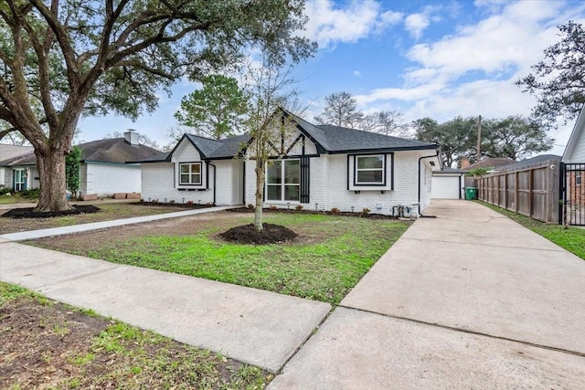 view of front facade featuring concrete driveway, fence, brick siding, and a front yard