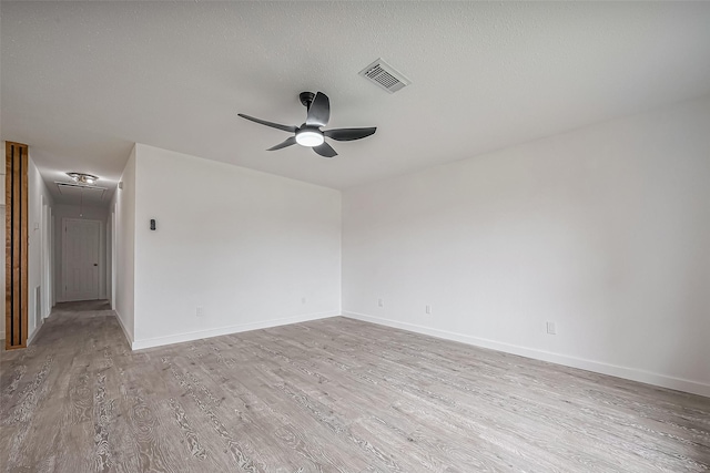 spare room with wood finished floors, baseboards, visible vents, attic access, and ceiling fan