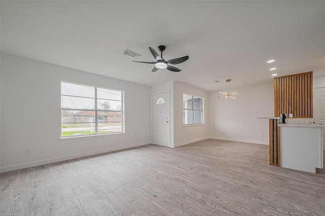 unfurnished living room featuring baseboards, visible vents, recessed lighting, ceiling fan with notable chandelier, and light wood-type flooring