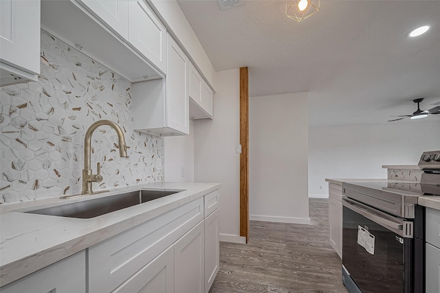 kitchen featuring stainless steel range with electric stovetop, wood finished floors, white cabinets, a ceiling fan, and a sink