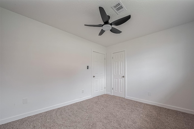 carpeted empty room featuring visible vents, a textured ceiling, baseboards, and ceiling fan