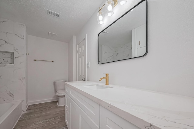 full bath featuring visible vents, toilet, a textured ceiling, wood finished floors, and vanity