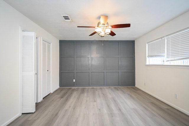 unfurnished bedroom featuring visible vents, a ceiling fan, light wood-style floors, a decorative wall, and baseboards