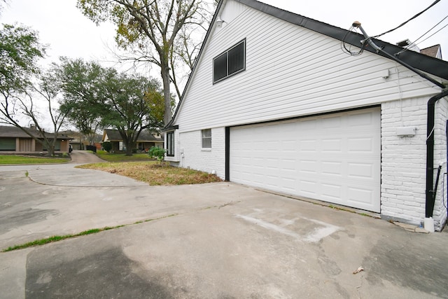 view of side of property with brick siding, an attached garage, and concrete driveway