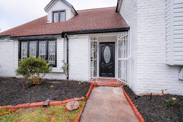 entrance to property featuring brick siding and a shingled roof