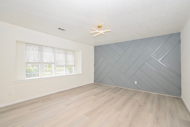 empty room with visible vents, an accent wall, baseboards, a chandelier, and light wood-type flooring