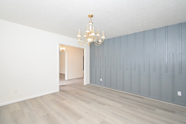 unfurnished room with baseboards, wood finished floors, a chandelier, and a decorative wall