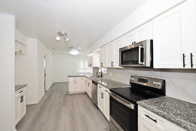 kitchen with a sink, tasteful backsplash, white cabinetry, appliances with stainless steel finishes, and light wood finished floors