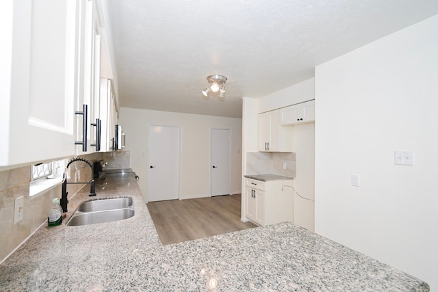 kitchen featuring a sink, backsplash, a textured ceiling, white cabinetry, and light stone countertops