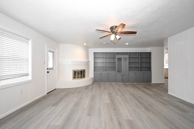 unfurnished living room featuring visible vents, a ceiling fan, a glass covered fireplace, light wood-style floors, and baseboards