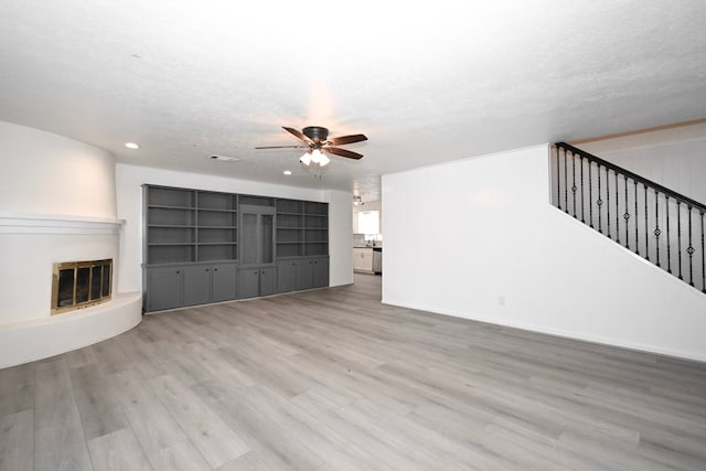 unfurnished living room with wood finished floors, a ceiling fan, stairs, a textured ceiling, and a large fireplace
