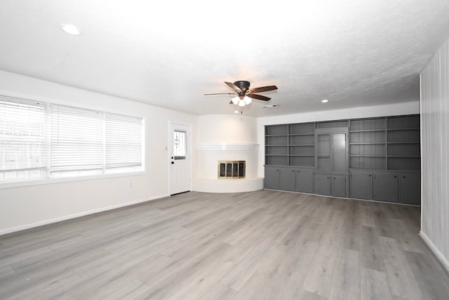 unfurnished living room with baseboards, light wood-type flooring, recessed lighting, a glass covered fireplace, and a ceiling fan