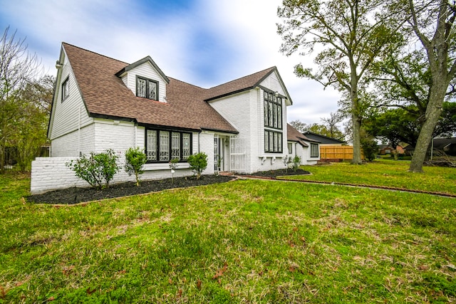 view of front of property with a front yard, fence, brick siding, and a shingled roof