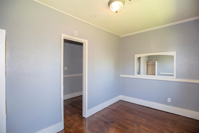 empty room featuring crown molding, dark wood-type flooring, and baseboards