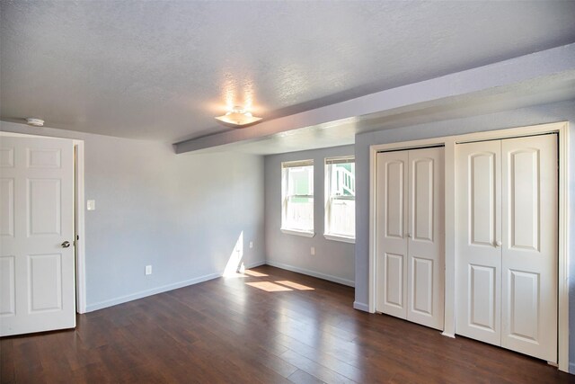 unfurnished bedroom featuring dark wood finished floors, a textured ceiling, two closets, and baseboards
