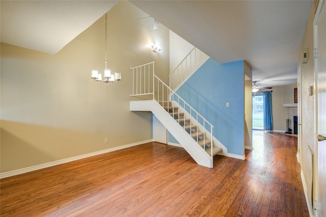 interior space with a fireplace with flush hearth, stairs, baseboards, wood finished floors, and ceiling fan with notable chandelier