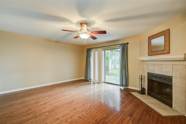 unfurnished living room featuring a ceiling fan, a tiled fireplace, wood finished floors, and baseboards