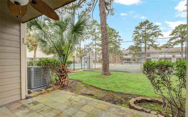 view of yard featuring a community pool, a patio area, central AC unit, a tennis court, and fence